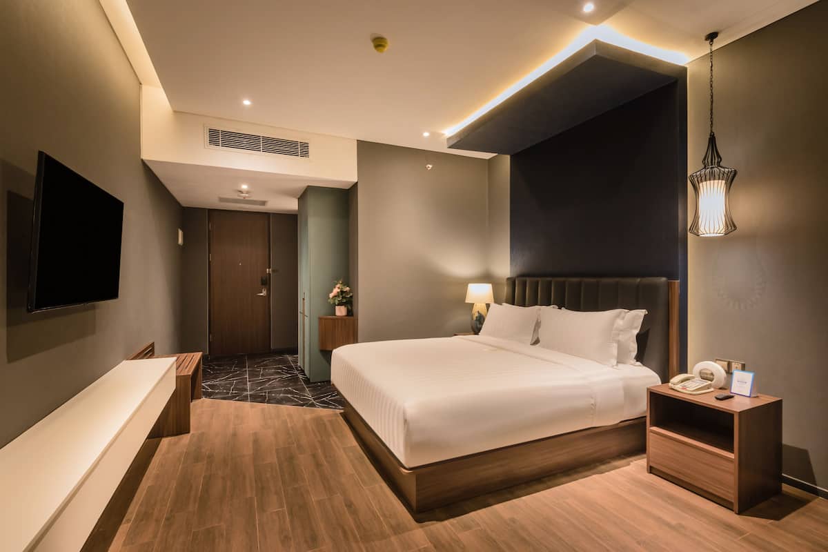 Une chambre d’hôtel moderne dotée d’un grand lit, de tables de chevet, d’un téléviseur à écran plat et d’une salle de bain avec un miroir et un lavabo.