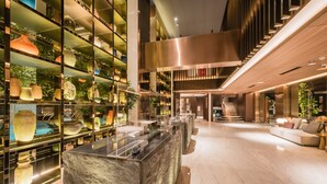 Eine moderne Lobby mit einer Marmorrezeption, Glastrennwänden mit Dekorationen, einer Treppe und einer Sitzecke.