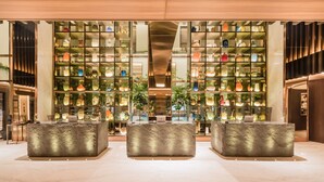 Eine moderne Lobby mit einer zentralen Rezeption, umgeben von einer Glasregalwand, die verschiedene dekorative Objekte zeigt.