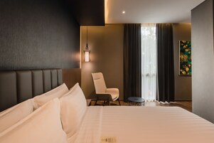 A modern hotel room with a large bed, a chair, a small table, and a painting on the wall.