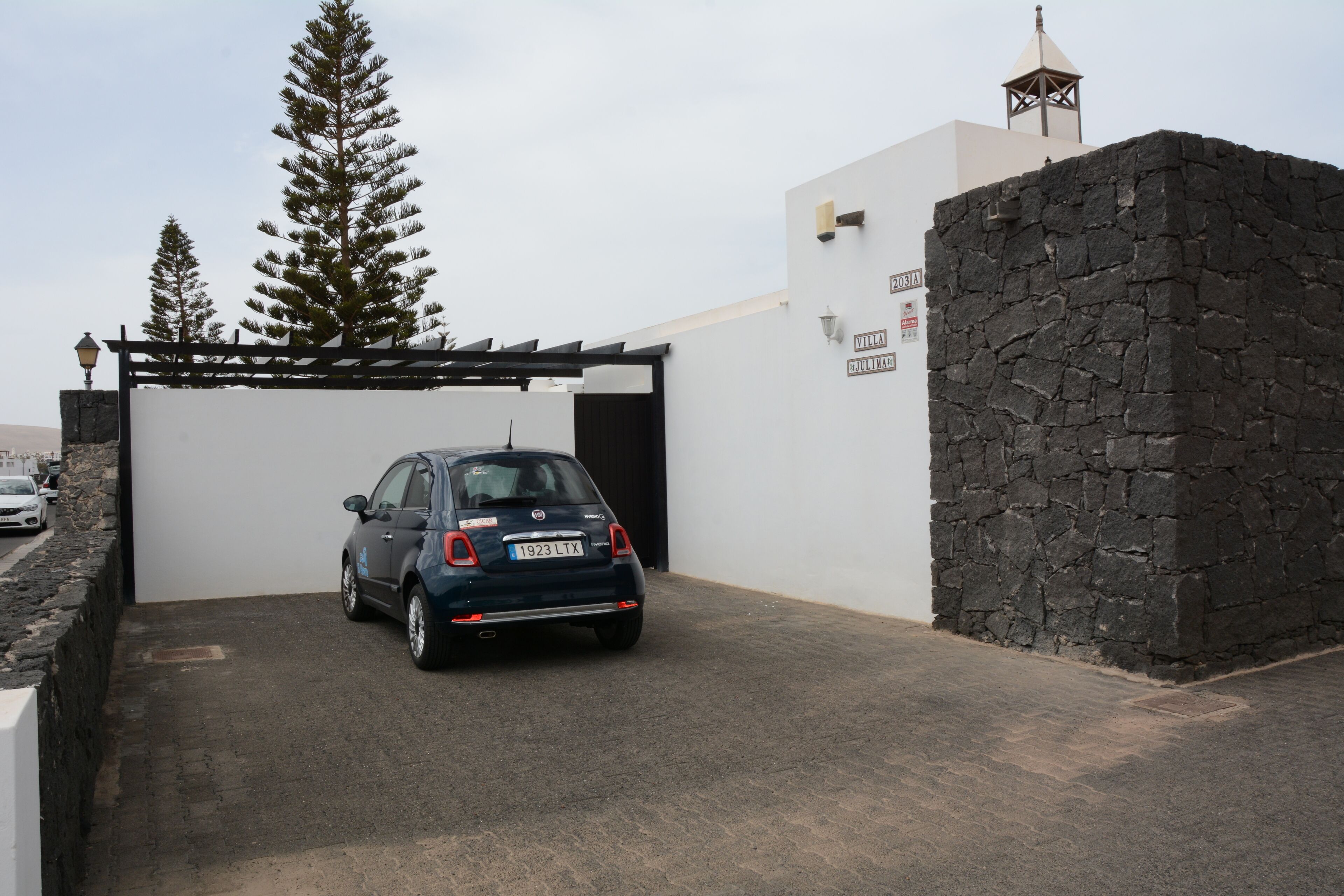 A car parked in a covered driveway with a stone wall and a pergola.