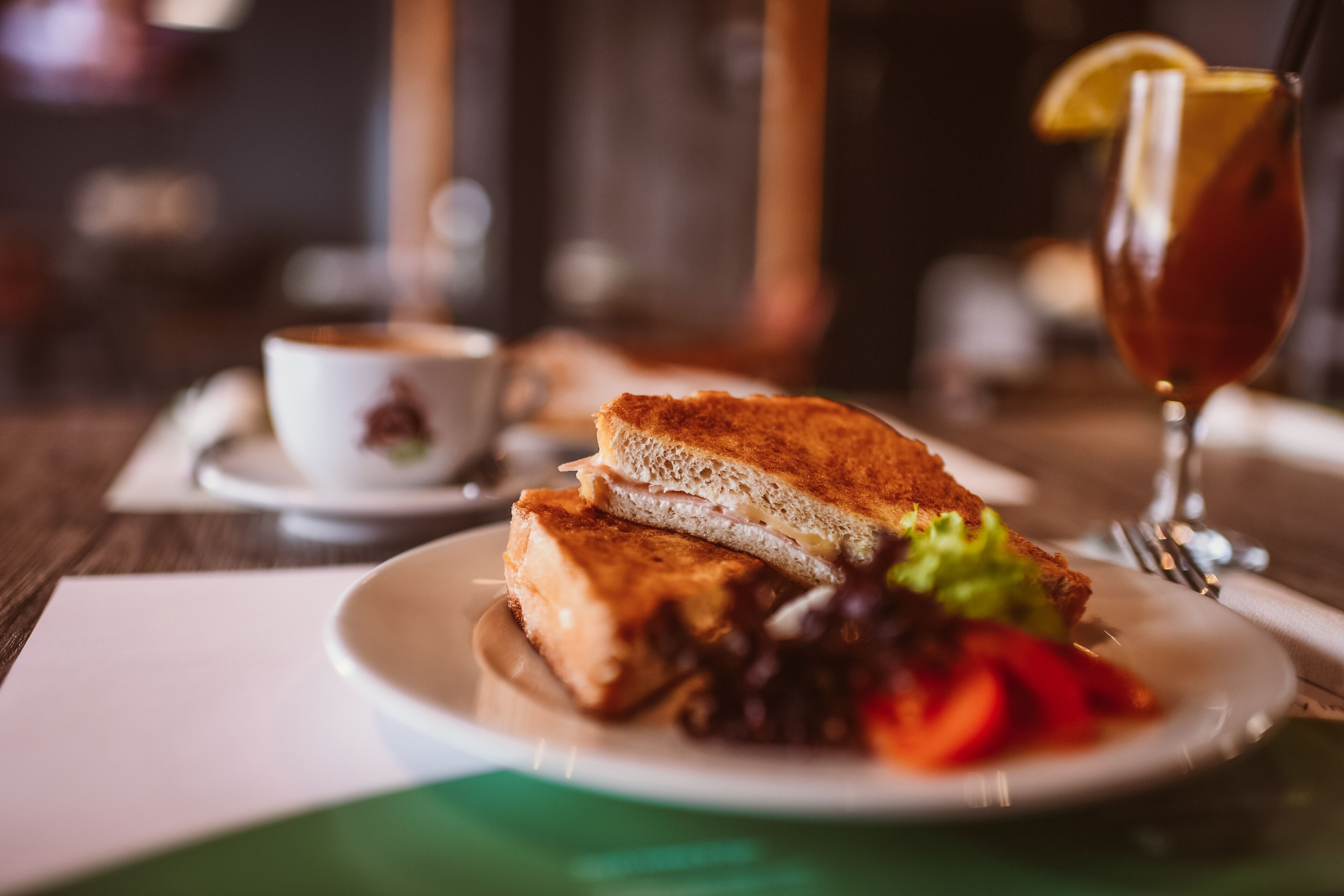 A sandwich with a side of vegetables and a glass of tea on a plate.