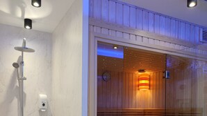 Une salle de bain moderne dotée d’un sauna en verre, d’une zone de douche séparée et d’un sol carrelé en marbre.