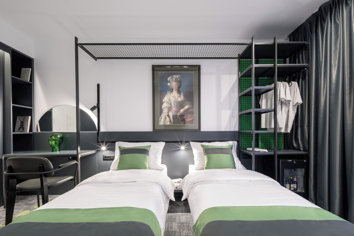 A modern hotel room with a bed, a desk, a chair, a shower, and a wardrobe.