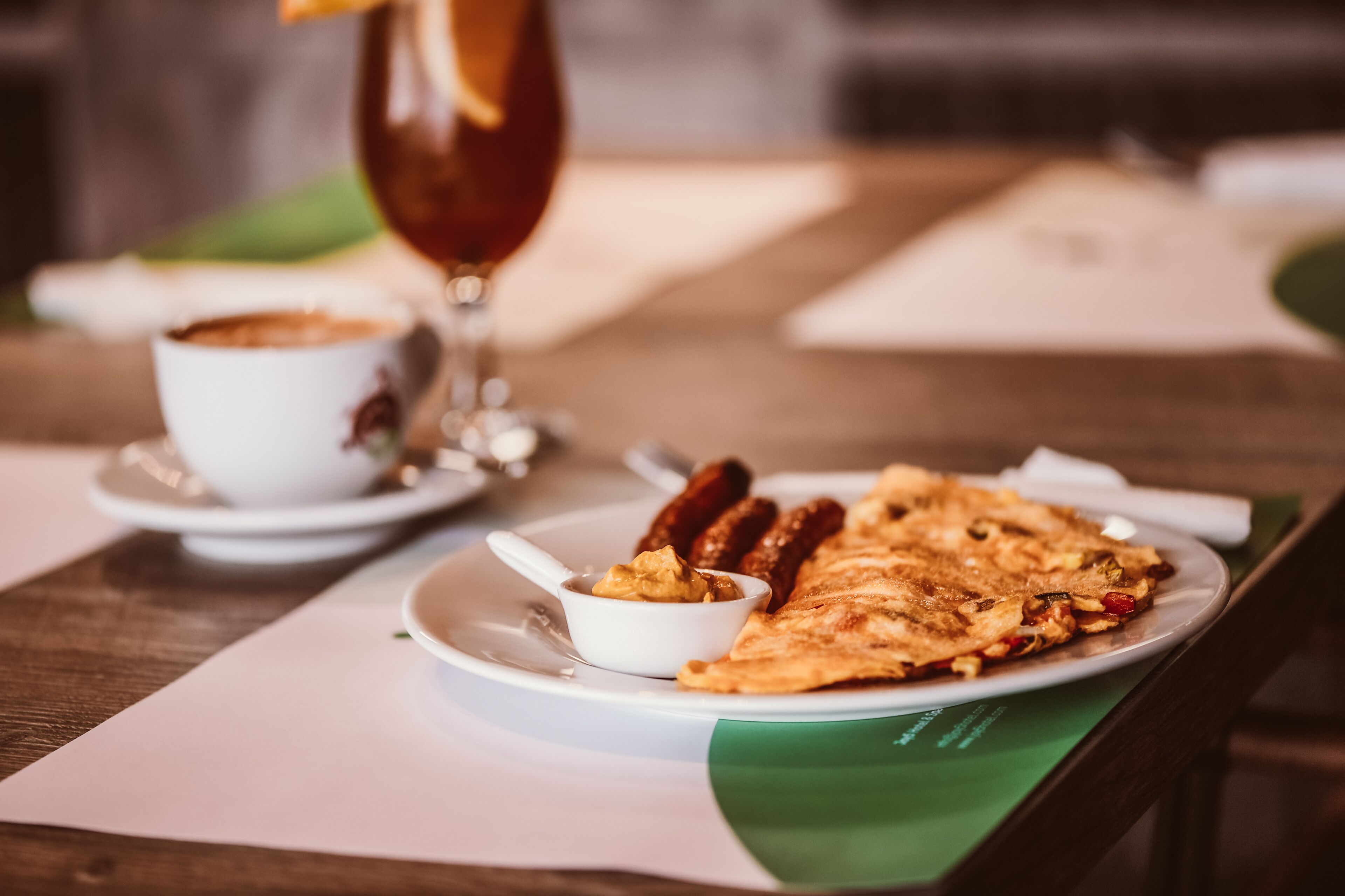 A dining table with a plate of food, a cup of coffee, and a glass of drink.