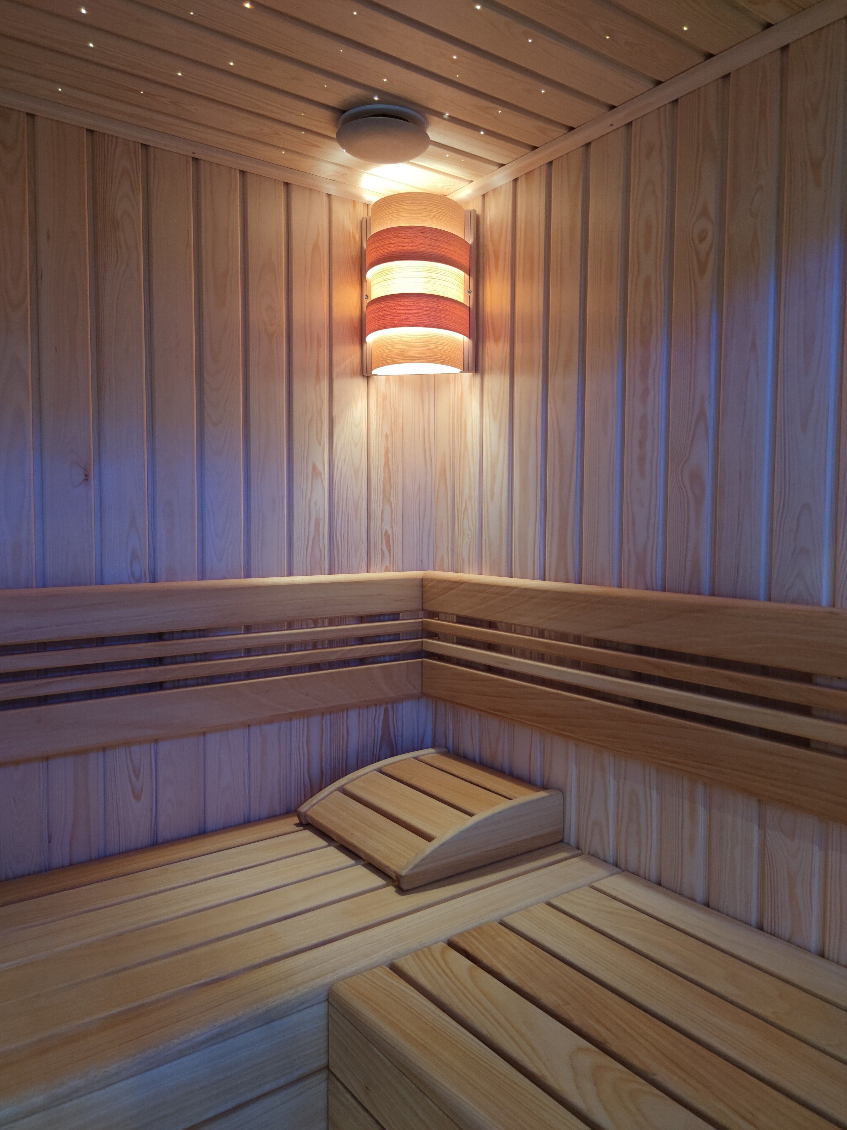 A wooden sauna with benches and a central light fixture.