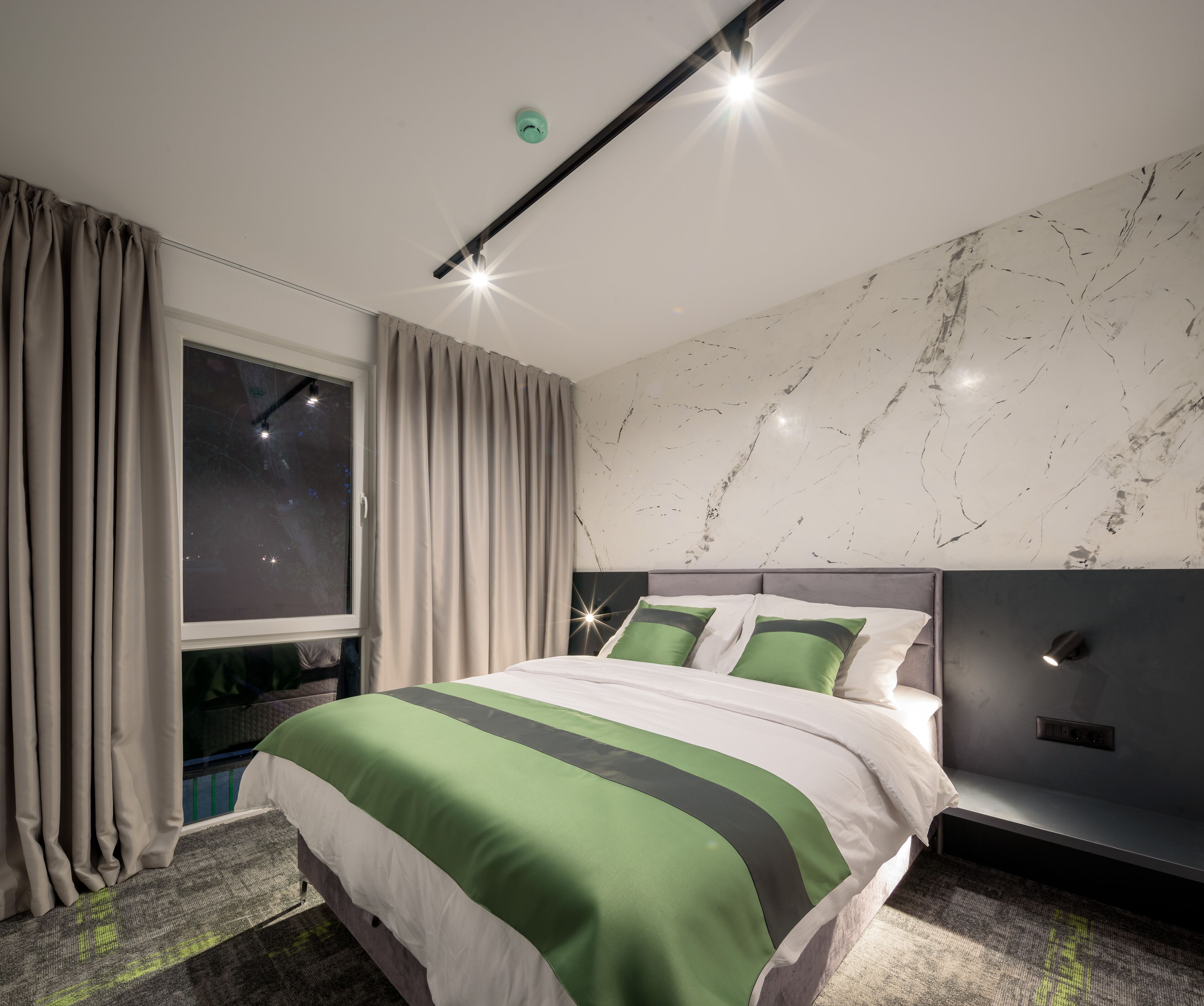A modern bedroom with a large bed, a headboard, a window with curtains, and a marble wall.