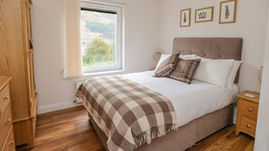 A bedroom with a bed, wooden wardrobe, a window with a view, and a bedside table. - Lochy Lookout (Spean Bridge)