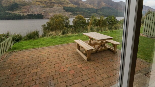 A picnic table on a brick patio with a view of a lake and mountains. - Lochy Lookout (Spean Bridge)