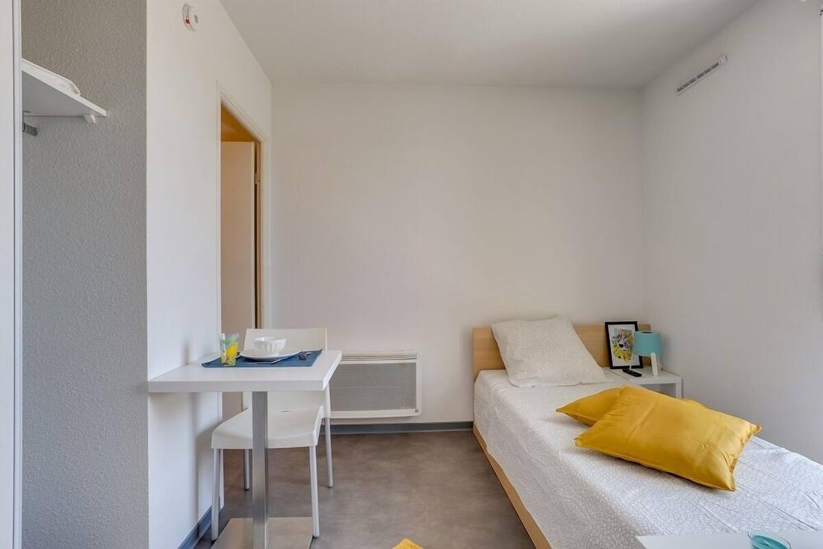 A small, clean room with a bed, a desk, and a chair.