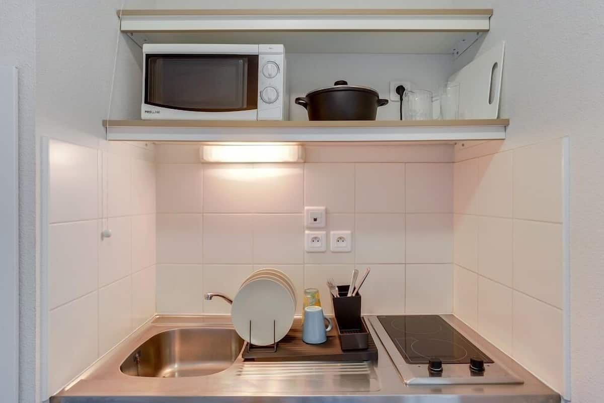 A compact kitchenette with a microwave, a pot, a sink, and a stove.