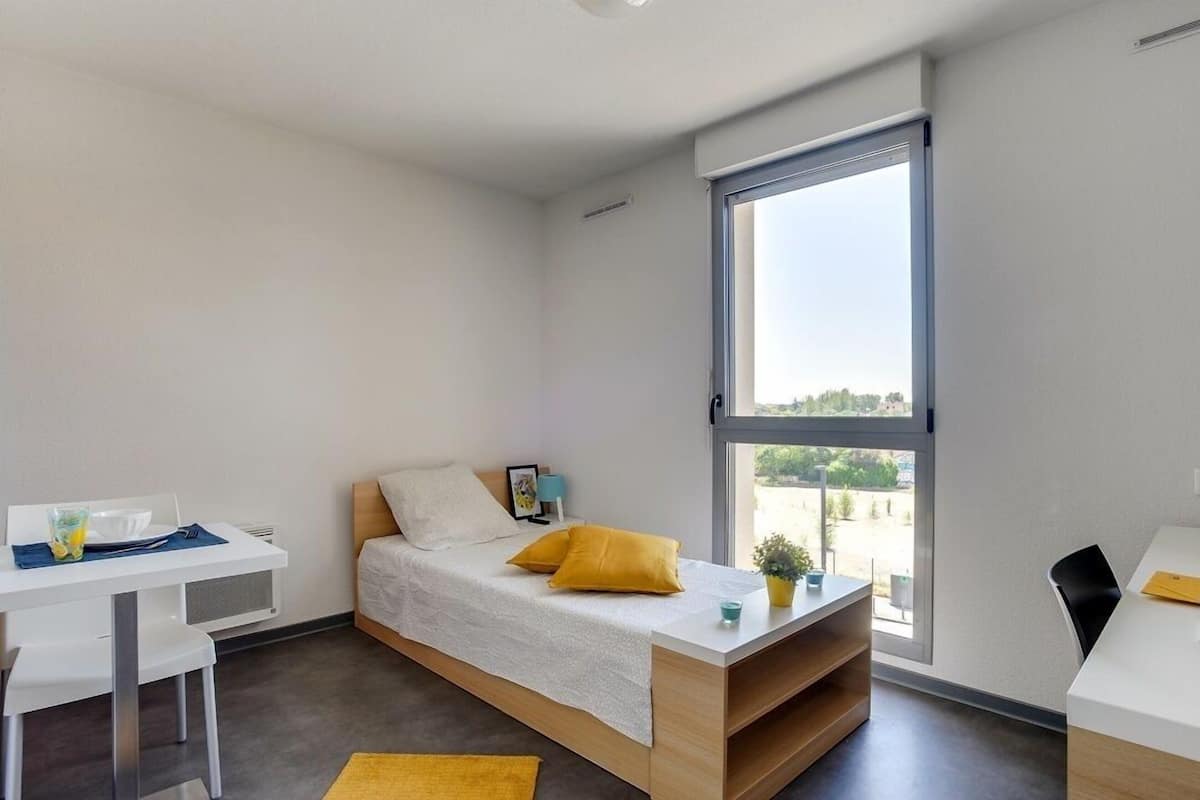 A compact room with a bed, a desk, and a window.
