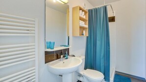 A bathroom with a white sink, a toilet, a mirror, and a shower with a blue curtain. - Apparteo Toulouse (Toulouse)