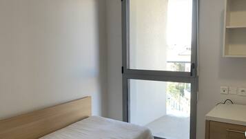 Ein kleines, sauberes Zimmer mit einem Einzelbett, einem Fenster, einem Nachttisch und einer kleinen Kommode.