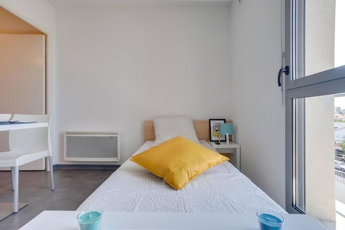A small, modern room with a bed, a desk, a chair, and a window.