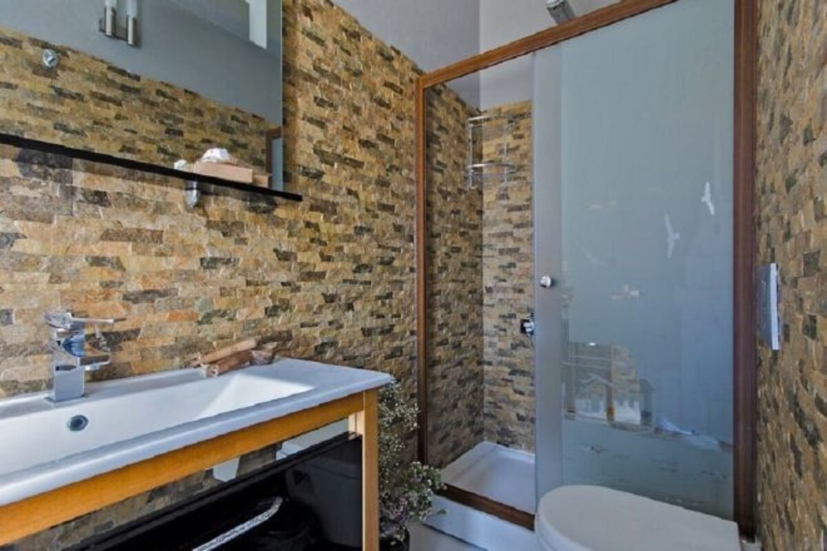 Un bany amb paret de pedra, una cabina de dutxa de vidre i un lavabo blanc.