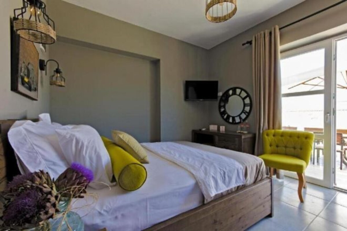 A bedroom with a bed, a television, a clock, a chair, and a window.