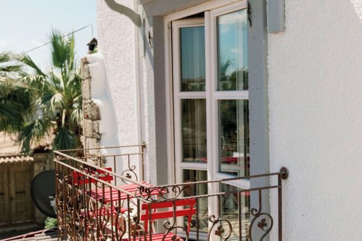 A balcony with a metal railing, a red bench, and a window with a white frame.