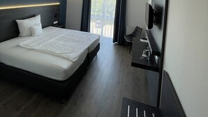 Ein modernes Hotelzimmer mit einem großen Bett, einem Schreibtisch, einem Flachbildfernseher und einem Balkon mit Vorhängen.