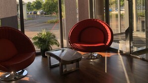 Eine moderne Lobby mit großen Fenstern, roten Stühlen und einem kleinen Tisch.