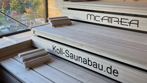 Ein moderner Saunaraum mit Holzbänken, beschriftet mit 'Koll-Saunabau.de' und 'McAIREA'.