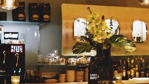 Eine Bar mit einer Kaffeemaschine, einer Flasche mit dem Aufdruck "LOST BOYS" und einer Vase mit Blumen.