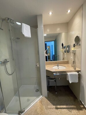 Une salle de bain moderne dotée d’une douche à parois de verre, d’un lavabo avec un plan de travail en granit et d’un miroir à cadre rond.