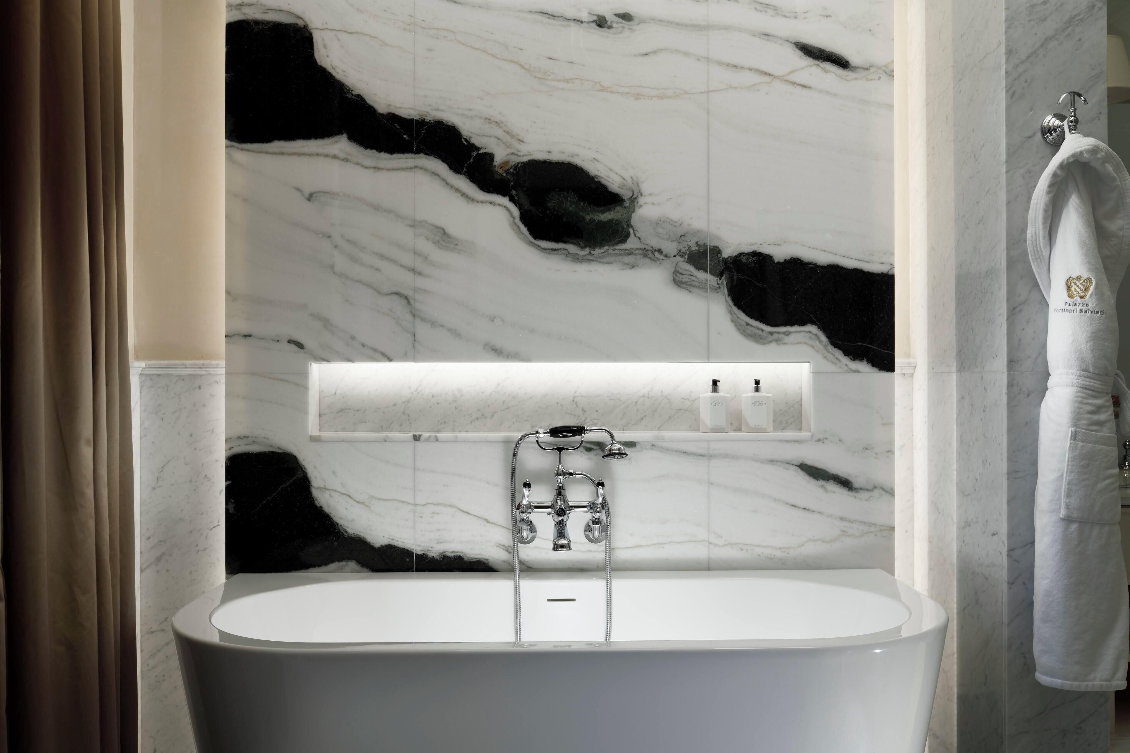 A modern bathroom with a marble wall, a white bathtub, and a towel hanging on the wall.
