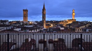 Vista de un paisaje urbano con torres destacadas y edificios históricos, tomada desde un balcón con barandilla de metal.