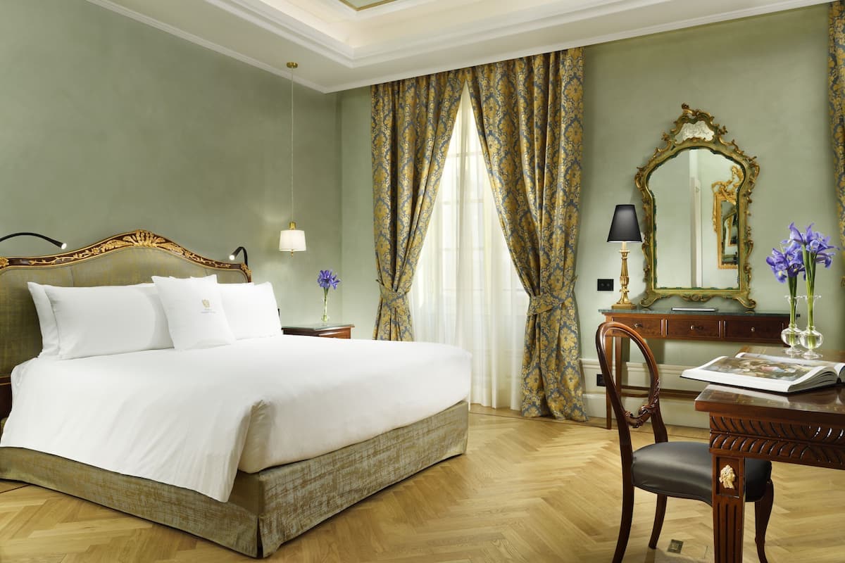Un dormitorio con una cama grande, un escritorio de madera, una silla, un espejo y cortinas.