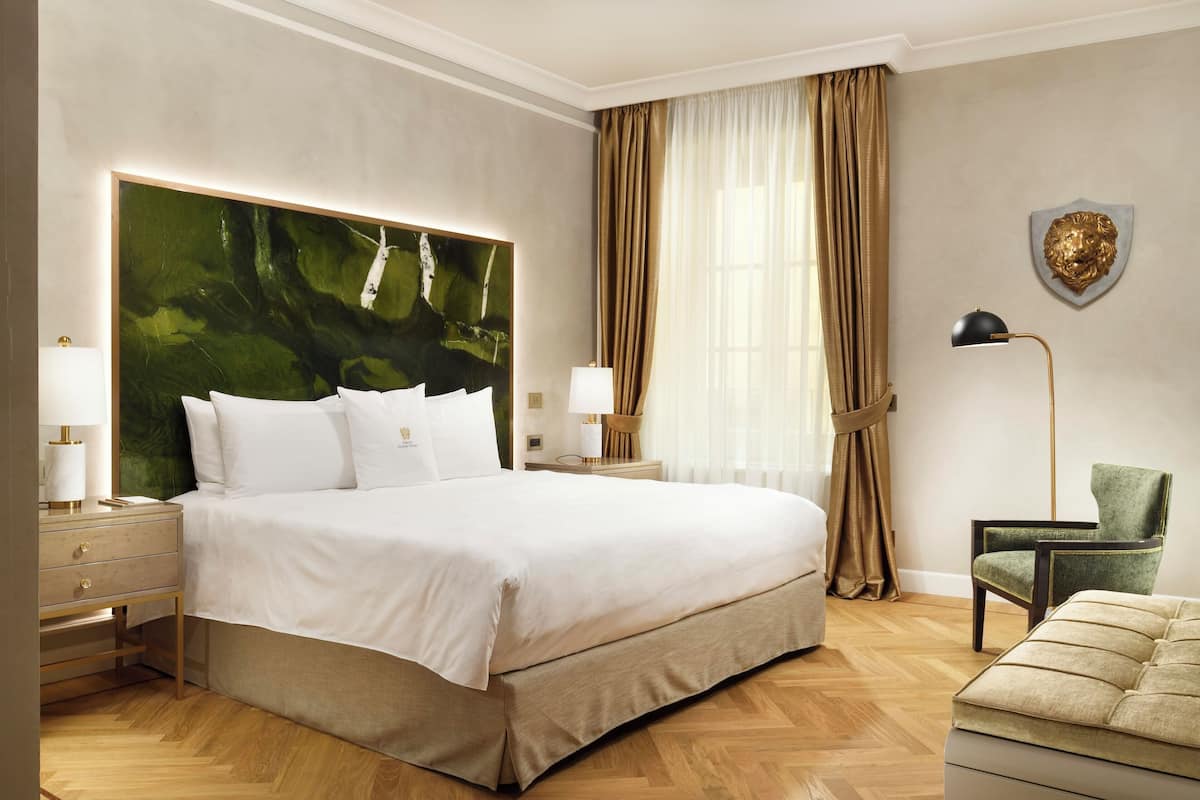 Un dormitorio amplio con una cama grande, una mesita de noche, un sillón verde y una lámpara de pie.