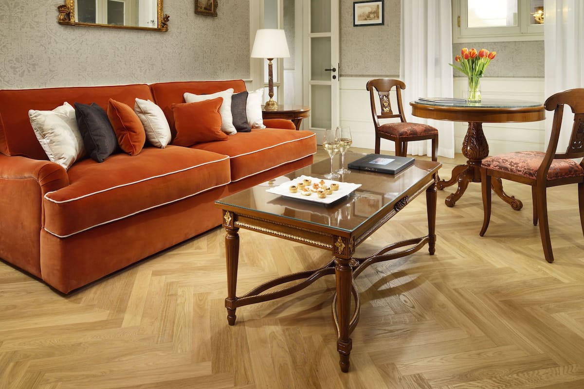 Un salón espacioso con suelo de madera en espiga, un sofá rojo con muchos cojines, una mesa de centro de cristal y una zona de comedor con mesa y sillas de madera.