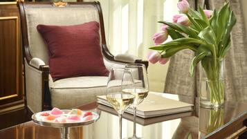 A room with a glass-top table, a chair with a cushion, a lamp, a vase with flowers, and a window with curtains.