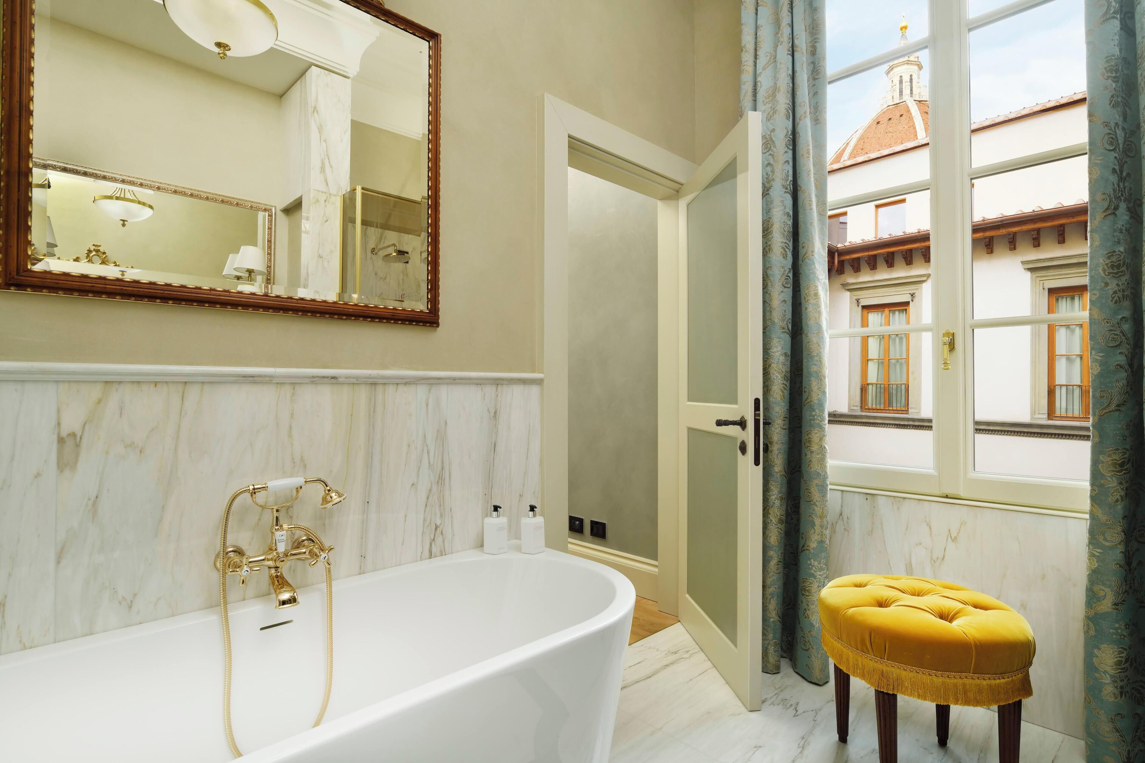 A bathroom with a freestanding bathtub, a large mirror, and a view of a building through an open door.