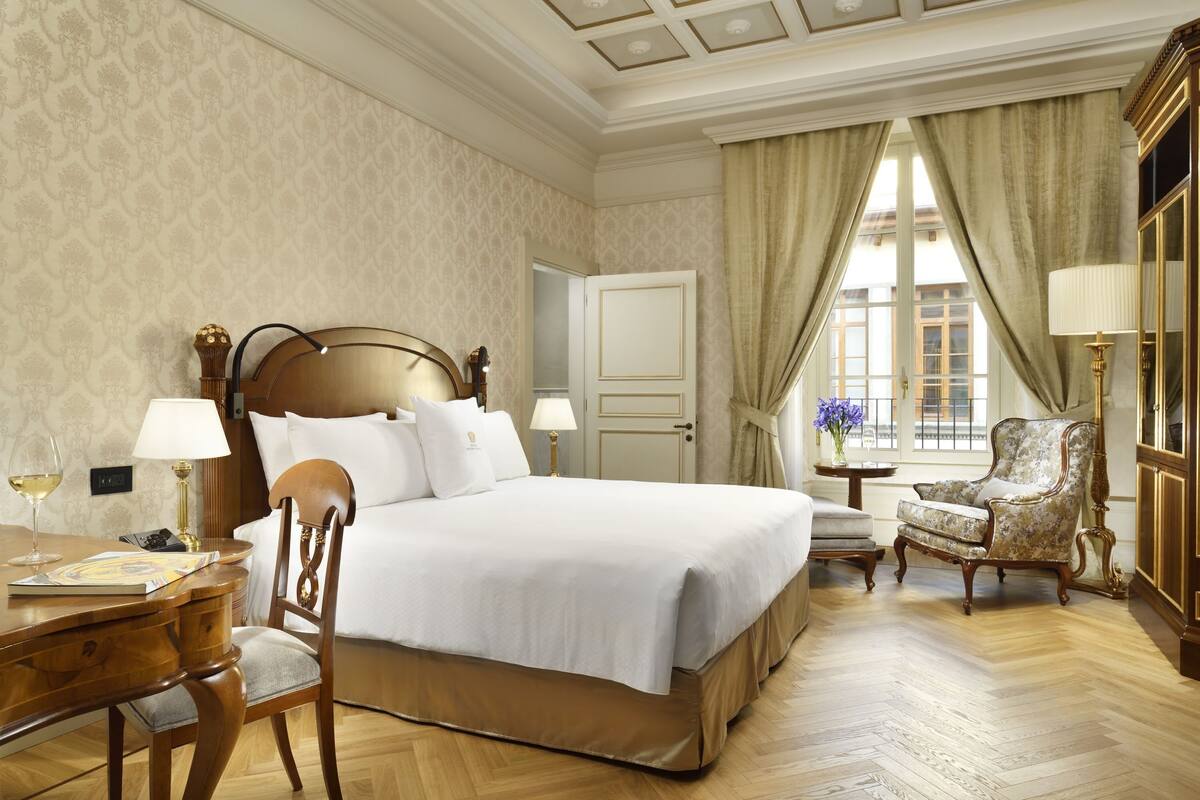 Una habitación de hotel con una cama grande, un escritorio de madera, una silla, una lámpara y vistas a la ciudad a través de la ventana.