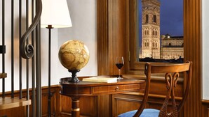 Un escritorio de madera con un globo terráqueo, un libro y una copa de vino. Una ventana muestra un edificio histórico al exterior.
