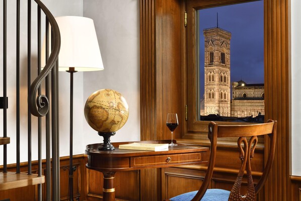 Un escritorio de madera con un globo terráqueo, un libro y una copa de vino. Una ventana muestra un edificio histórico al exterior.