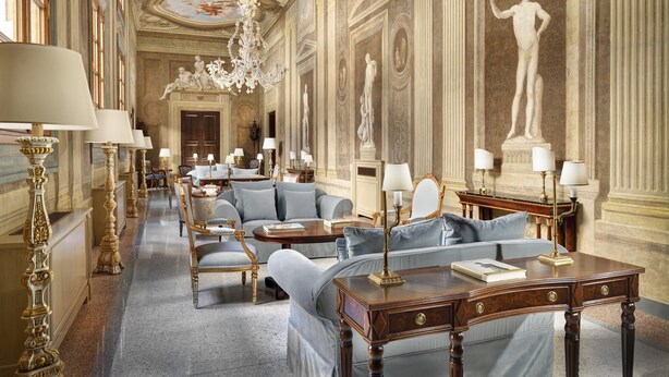 Un lobby de hotel lujoso con candelabros ornamentados, estatuas clásicas y muebles elegantes.