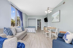 Un salon moderne comprenant un canapé, une table à manger avec des chaises, un lit et un téléviseur fixé au mur.