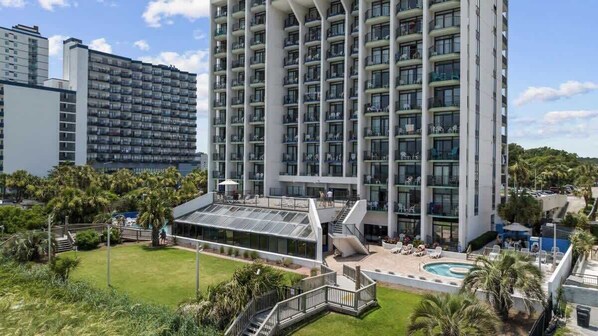 A high-rise hotel with multiple balconies, a swimming pool, and a well-maintained lawn area.