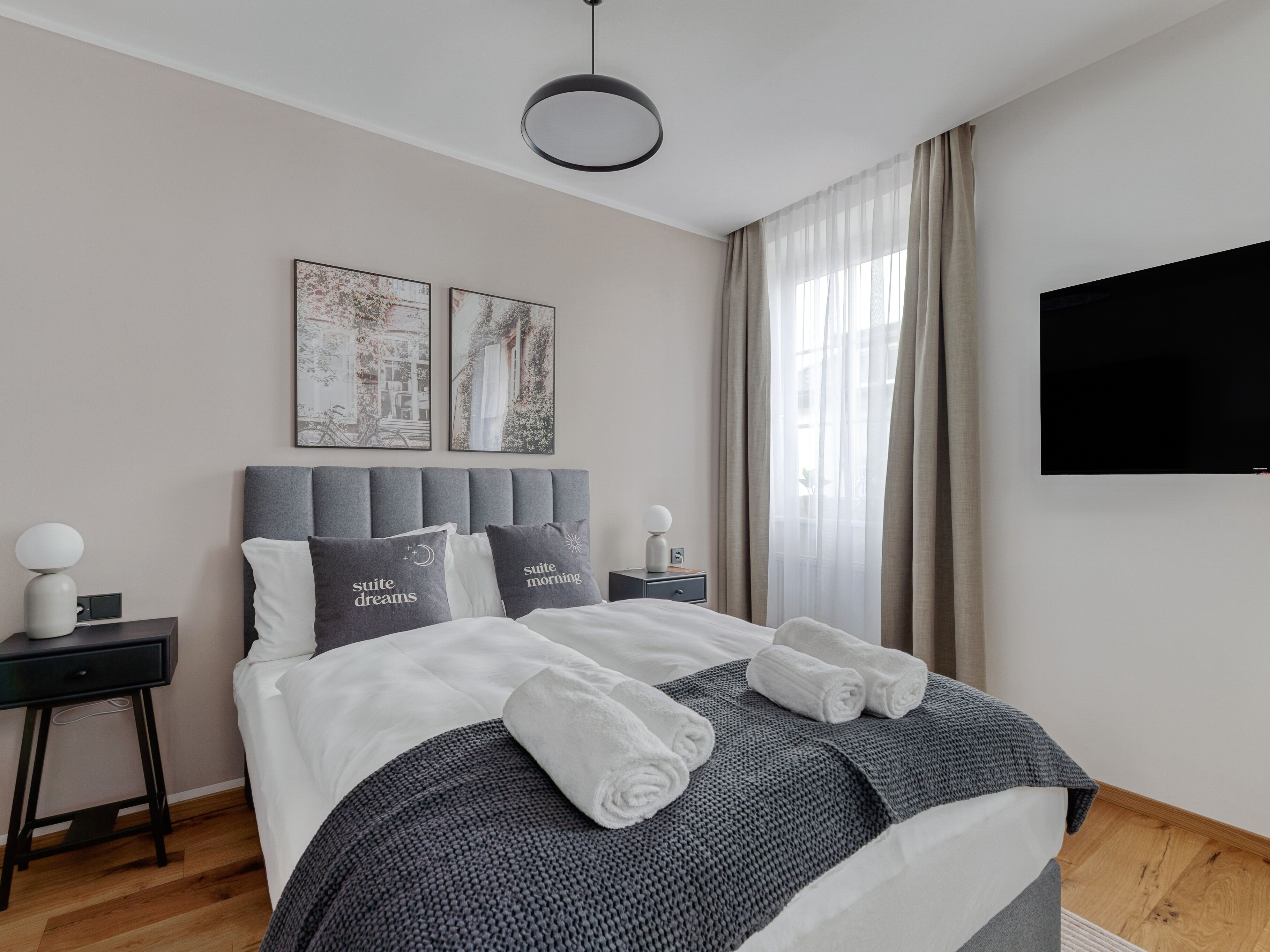 Una habitación de hotel moderna con una cama bien hecha, una mesita de noche con una lámpara y dos cuadros en la pared.