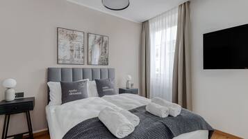Una habitación de hotel moderna con una cama bien hecha, una mesita de noche con una lámpara y dos cuadros en la pared.