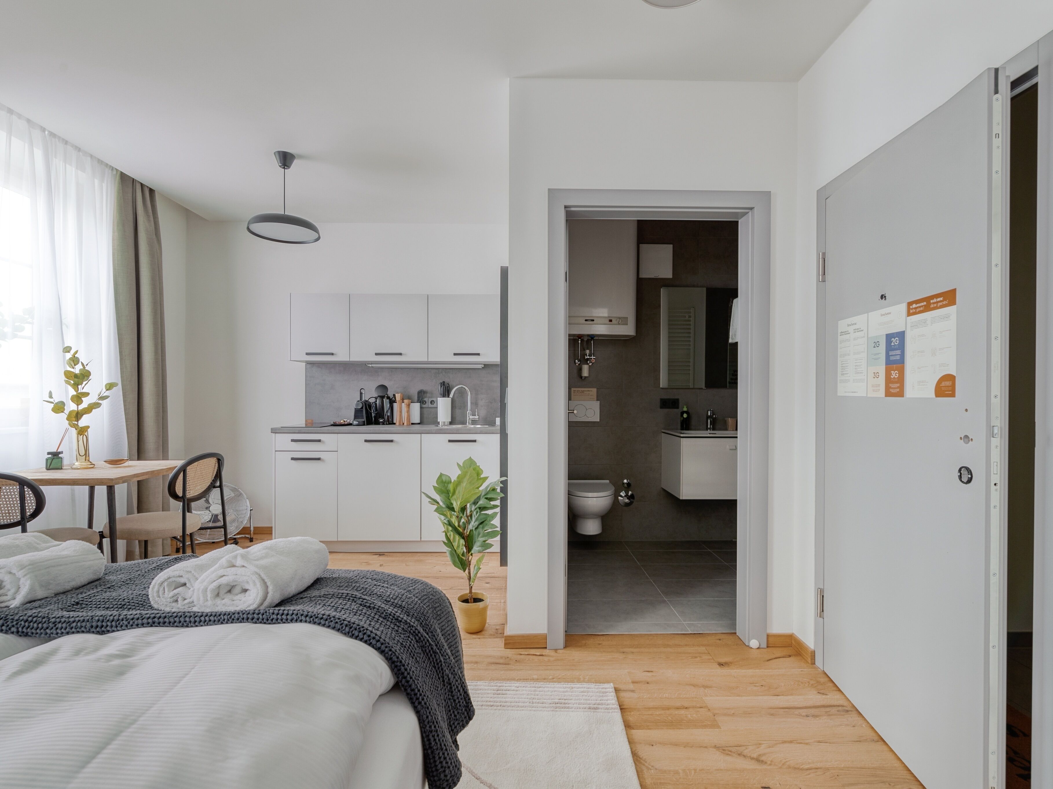 A modern hotel room with a bed, a small dining area, a kitchen, and a bathroom.