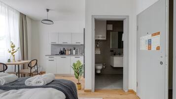 A modern hotel room with a bed, a small dining area, a kitchen, and a bathroom.