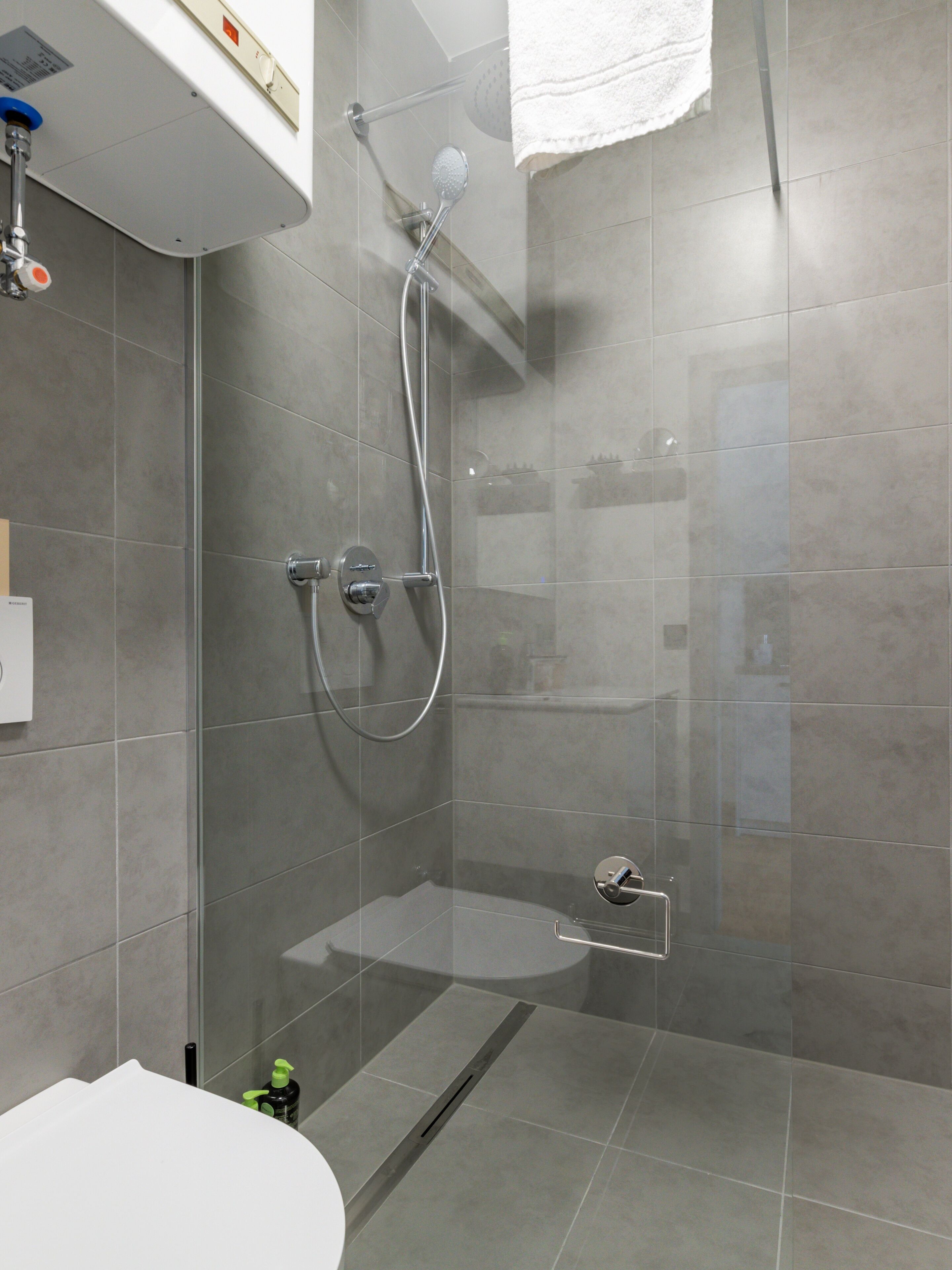 Une douche moderne dotée d’un pare-douche en verre, d’un pommeau de douche à main et d’un flexible de douche.