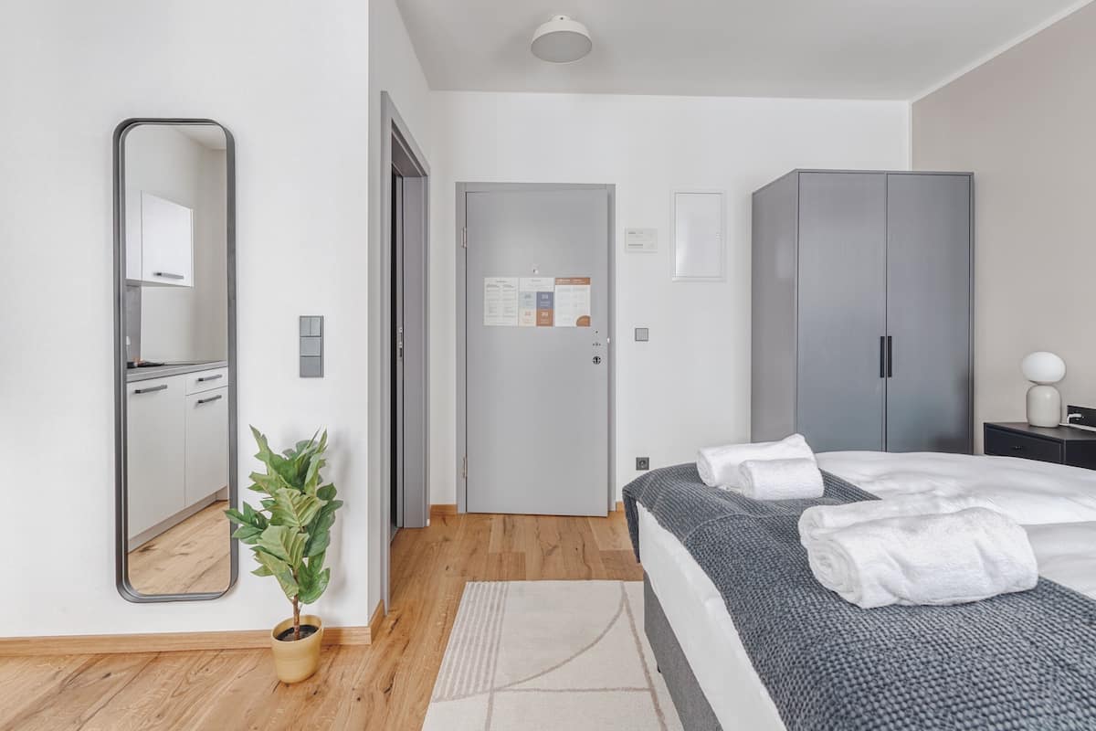 Een moderne slaapkamer met een bed, een kledingkast, een spiegel en een potplant.
