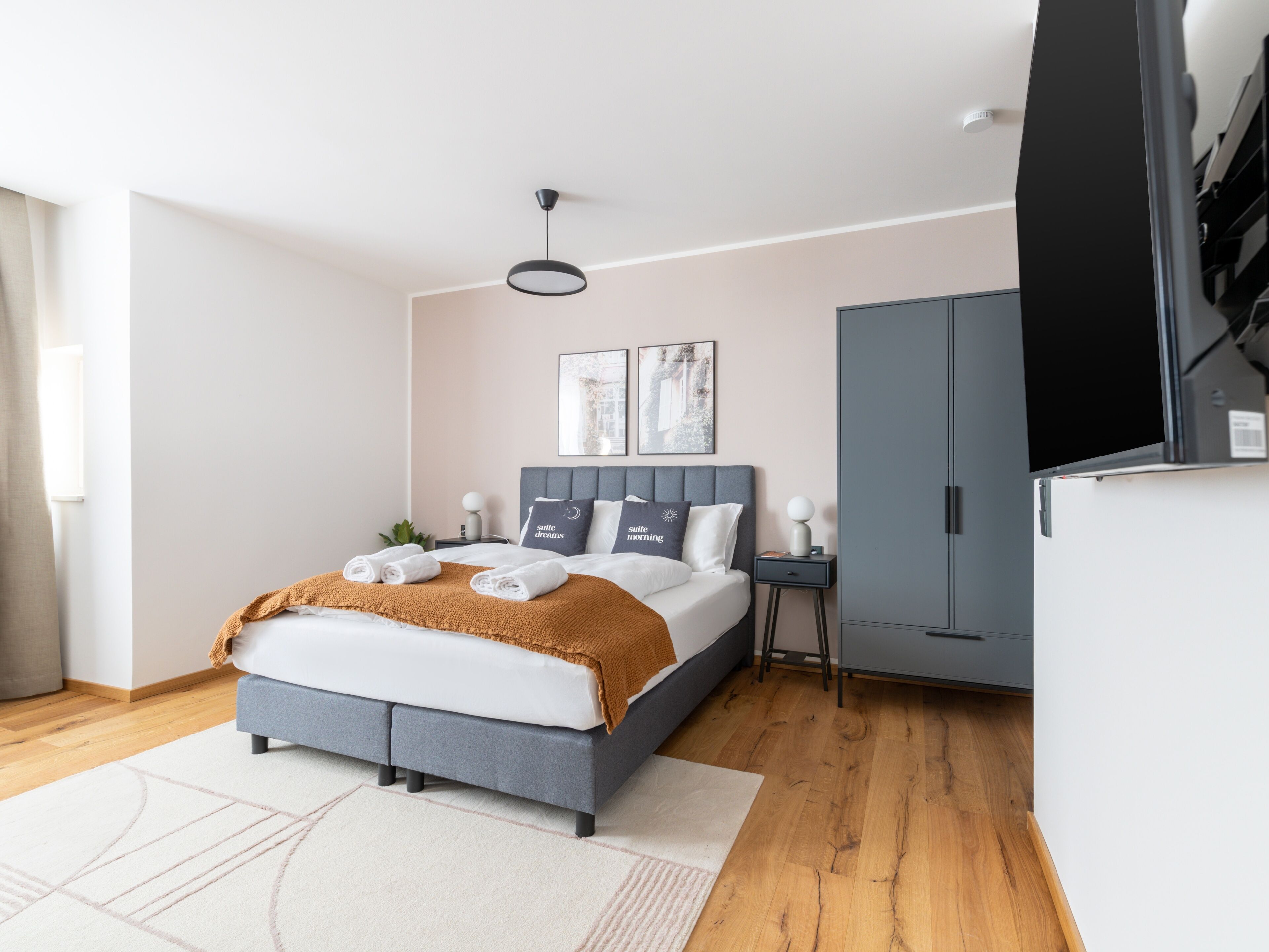 Un dormitorio moderno con cama, mesitas de noche, armario y una obra de arte en la pared.