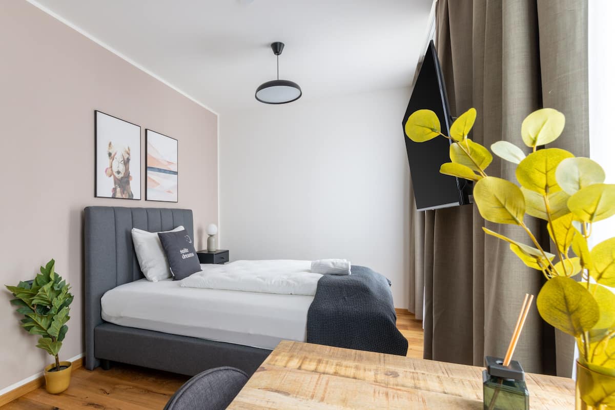 Een moderne slaapkamer met een bed, nachtkastje, lamp en een kamerplant.