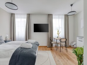 A modern hotel room with a large bed, a desk with two chairs, a flat-screen TV, and a small table with a plant. - Limehome Villach Gerbergasse (Villach)