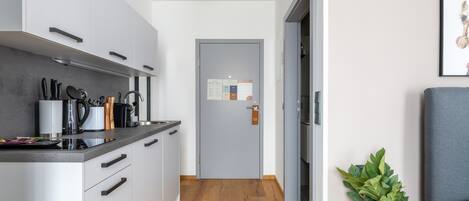 A modern kitchen with grey cabinets, a wooden floor, and a small plant by the door.